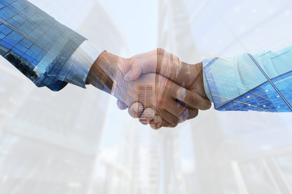 Two business professionals shaking hands in front of a modern office building, symbolizing a successful partnership.